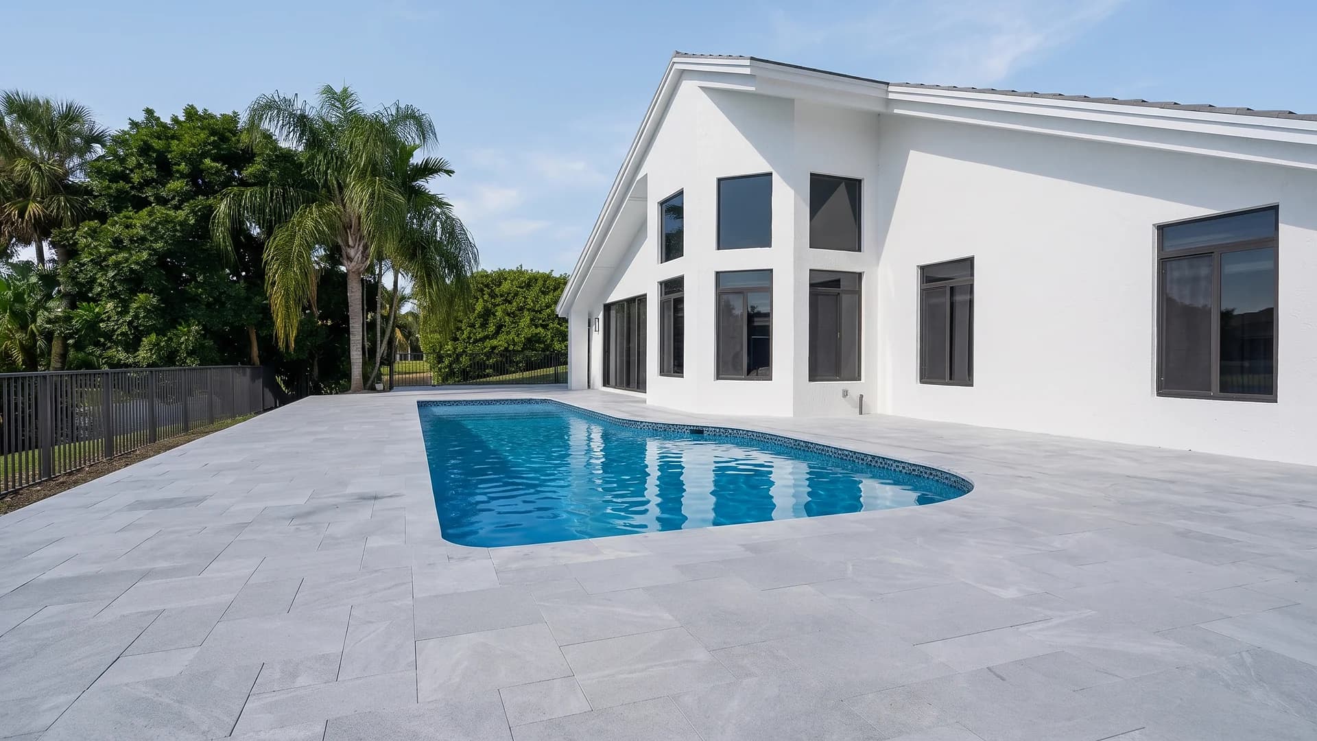 Stone paver pool deck next to a modern white home